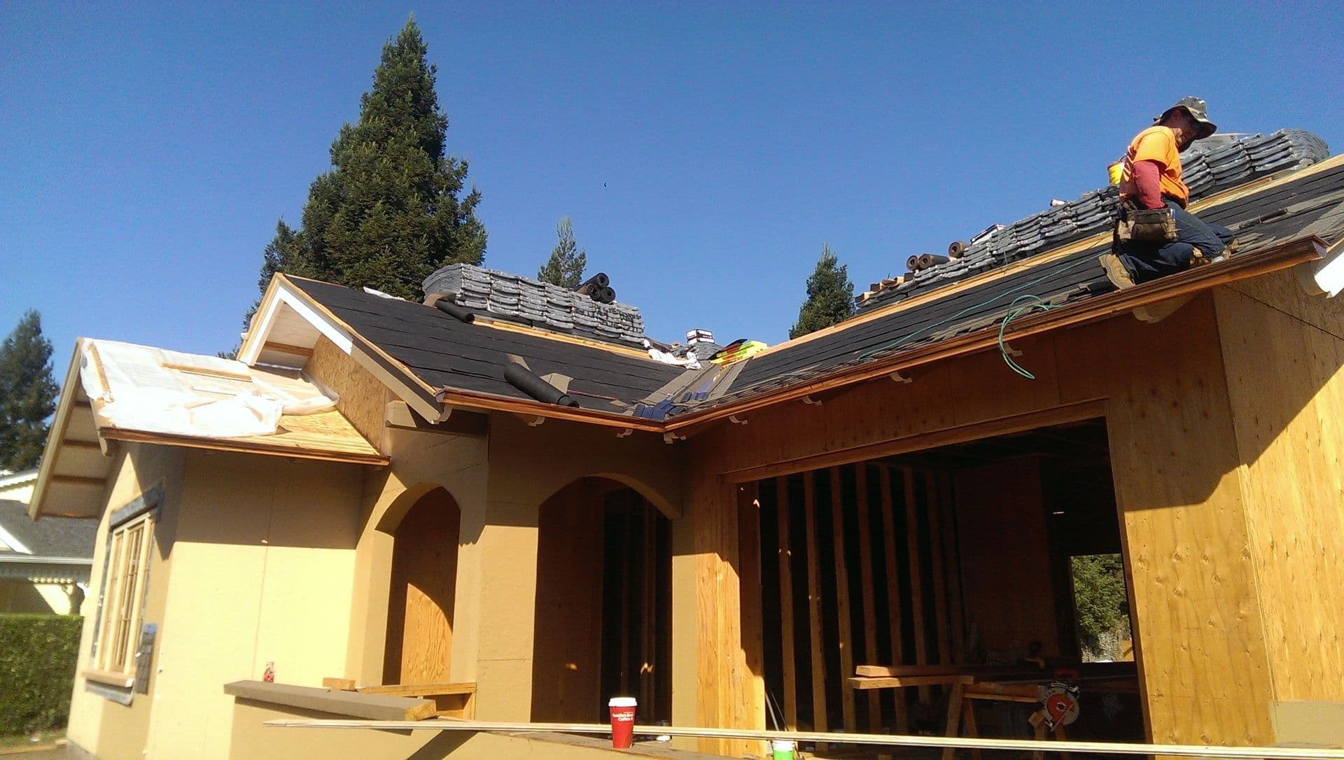 Roofers installing shingles on a house under construction against a clear blue sky.