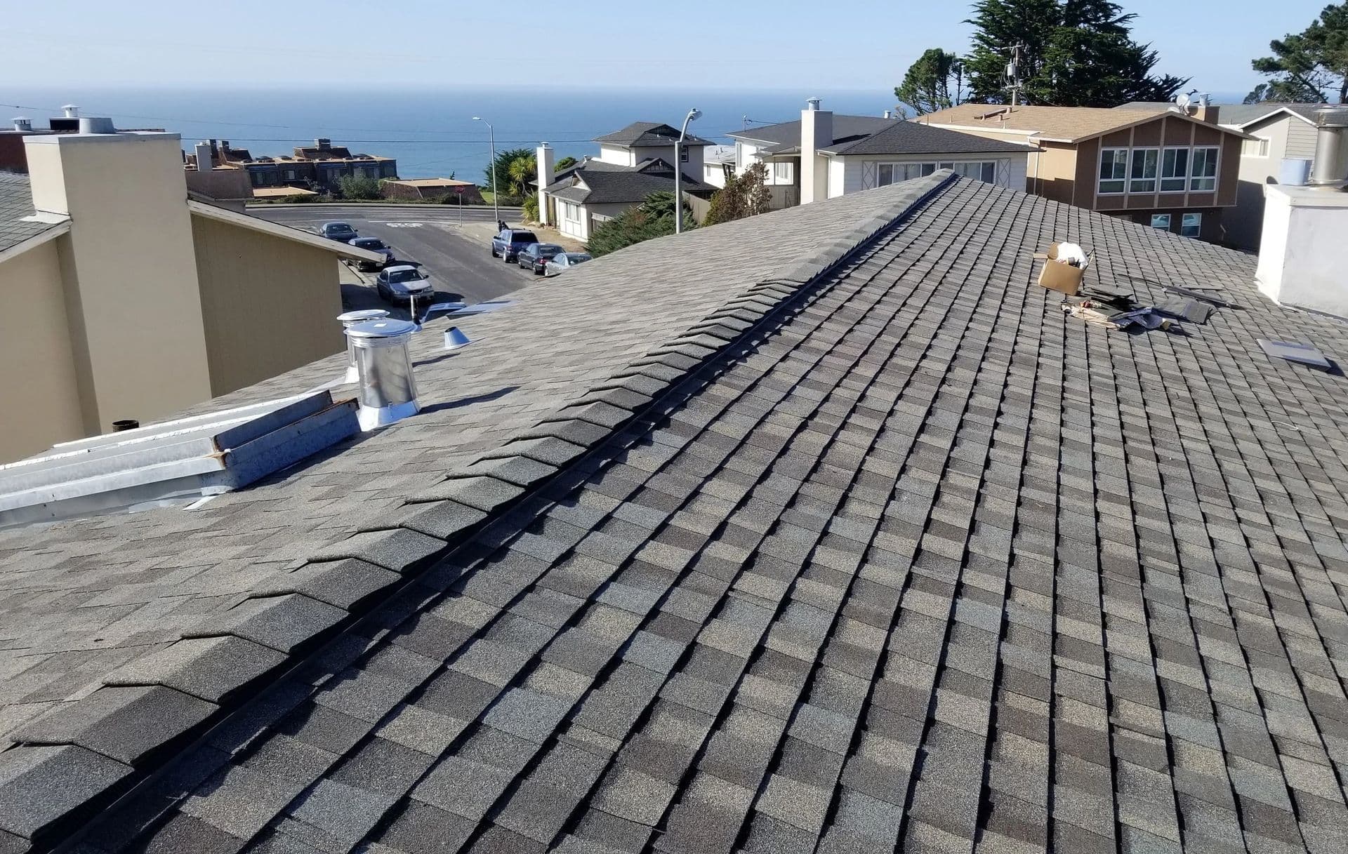 Roofing installation above coastal homes with ocean view and clear sky.