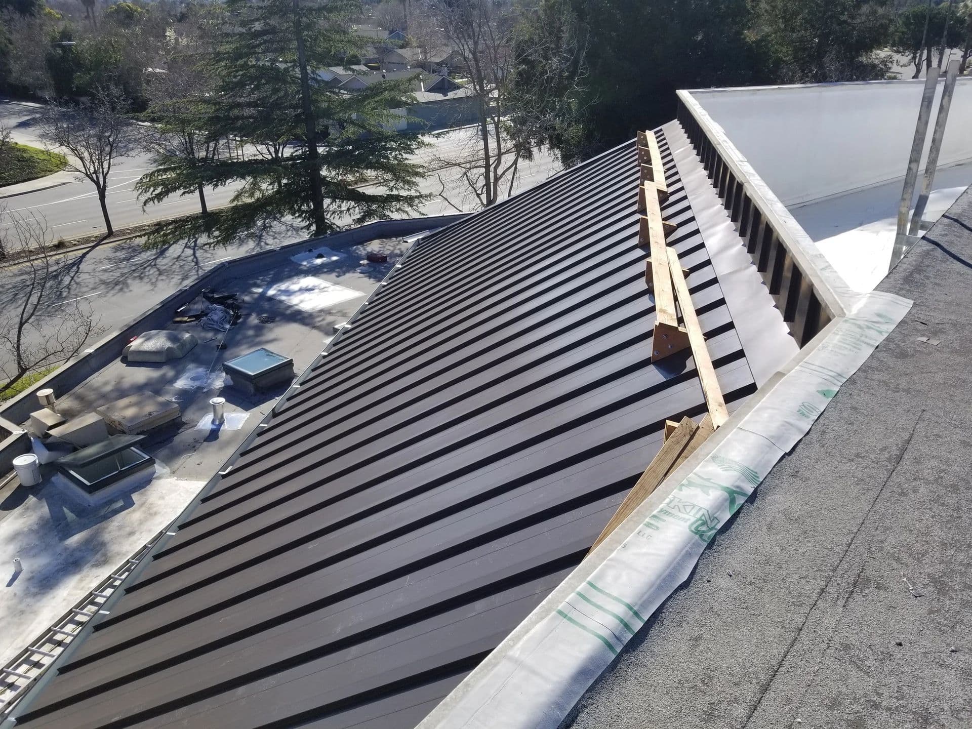 Aerial view of a metal roof under construction, showcasing roof panels and surrounding landscape.