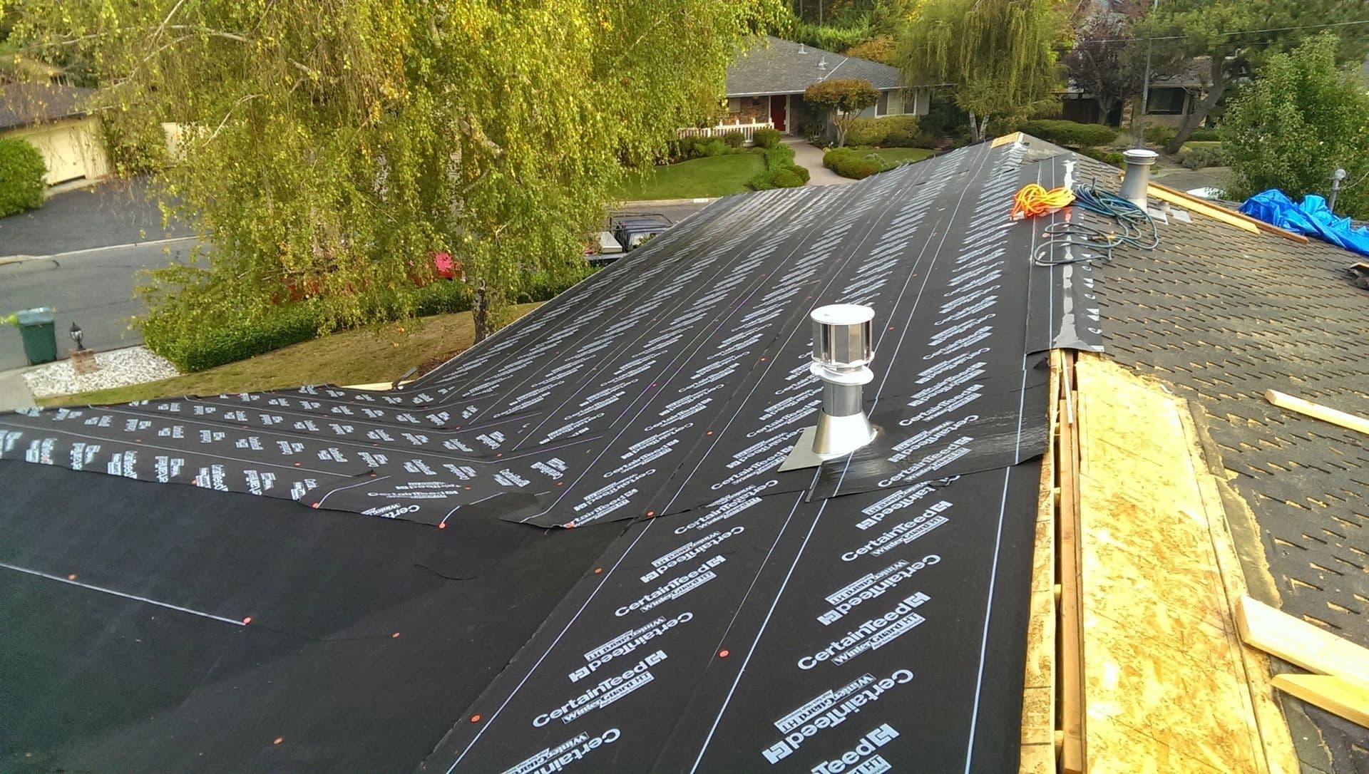 Roofing installation with black underlayment and ventilation pipe on a residential home.